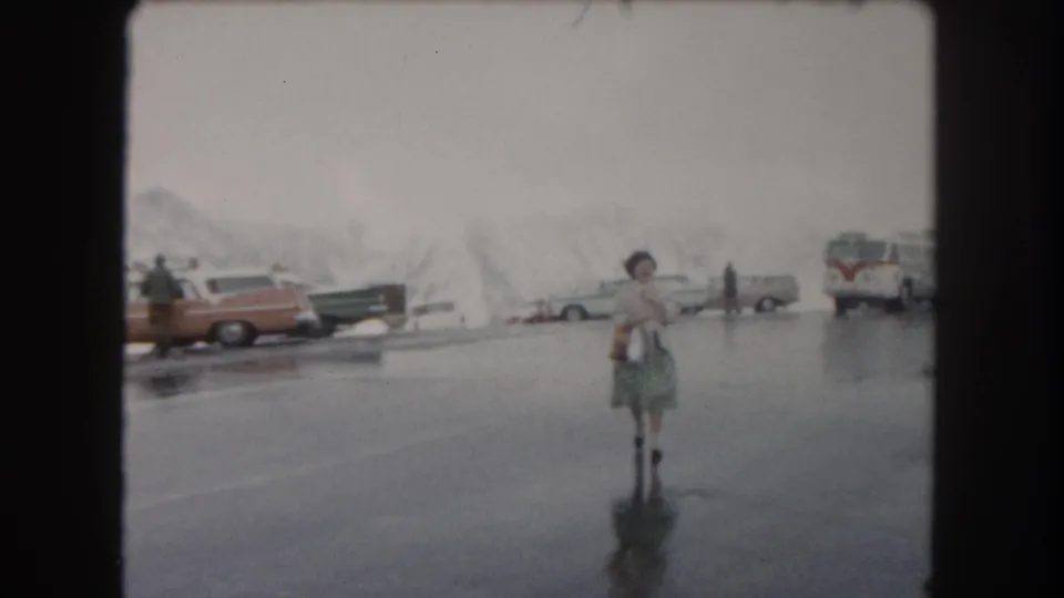 The woman moves closer through the Summit County parking lot, carrying a bag as cars, a bus, and icy snowbanks sit behind her.