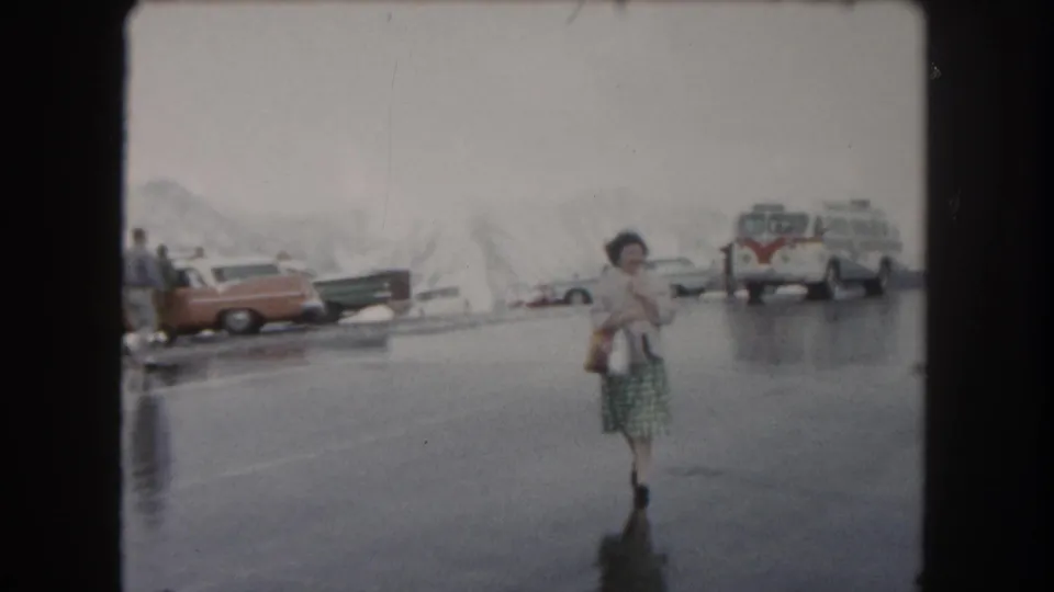 A woman in a light jacket and patterned skirt walks toward the camera across slick pavement in a snowy Summit County parking area.