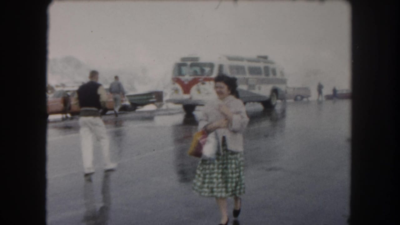 Woman in a checkered skirt smiles in a wet parking lot near a red-and-white tour bus.