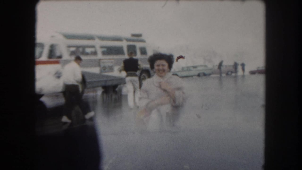 A woman smiles toward the camera in 1962 Summit County, Colorado, with a tour bus and travelers behind her.