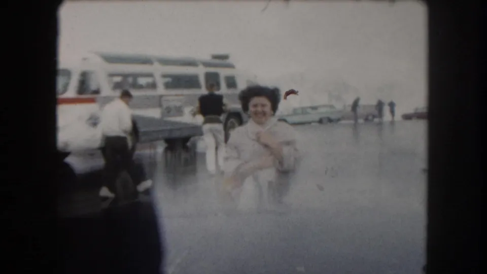 A woman smiles toward the camera in 1962 Summit County, Colorado, with a tour bus and travelers behind her.