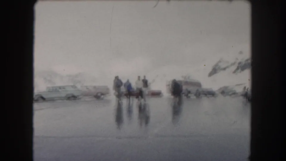 A wider 1962 Summit County, Colorado view shows travelers, parked vehicles, wet pavement, and snowy mountain slopes.