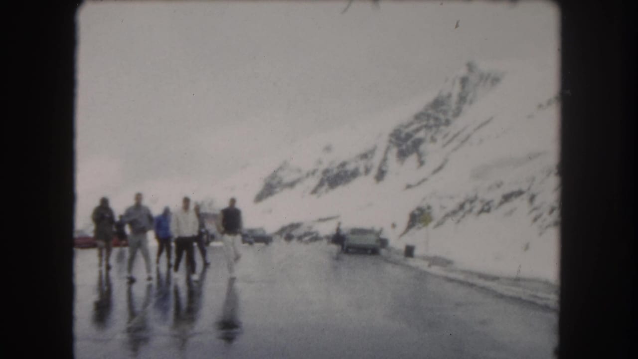 People in winter clothing walk along reflective pavement in Summit County, Colorado, with snowbanks and parked vehicles nearby.