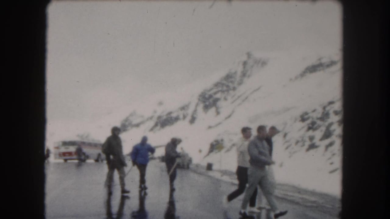 People stand and walk on a wet snowy mountain road near a bus and car.