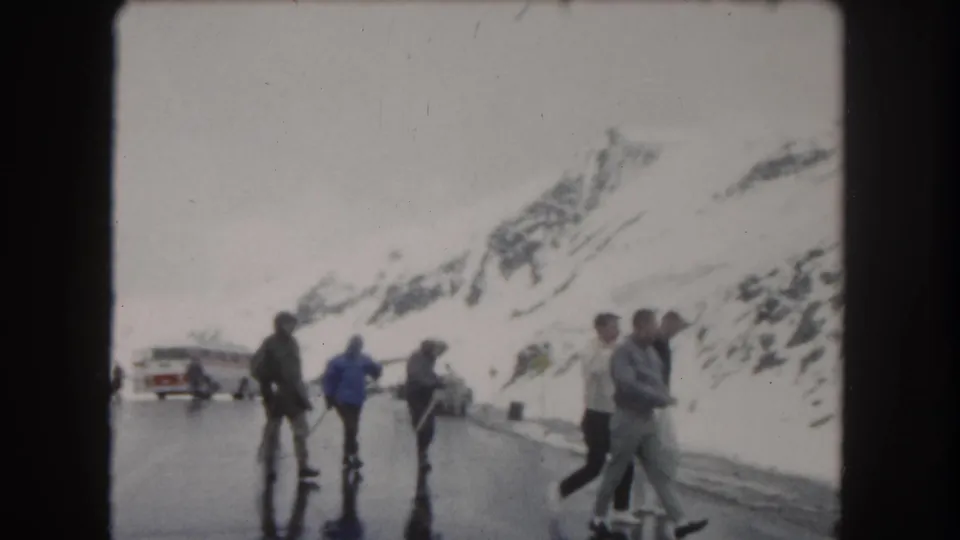 Travelers in winter clothing pause on a wet road in snowy Summit County, Colorado, with a bus, car, and mountain slopes nearby.