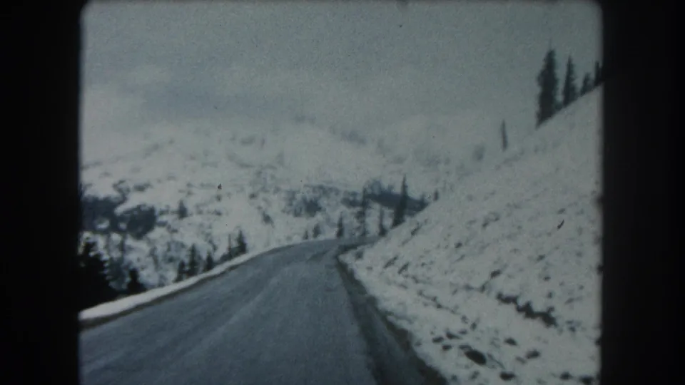 The road-view perspective looks down a wet mountain road bordered by snow, evergreen trees, and pale winter slopes in Summit County.