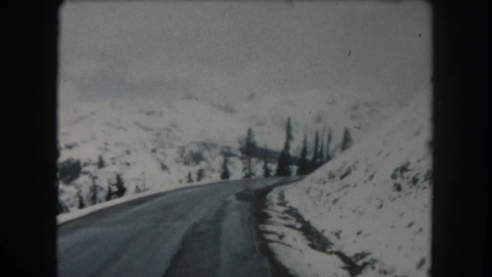 1962 Summit County, Colorado home-movie frame showing a winding snowy road and evergreen trees along a mountain slope.