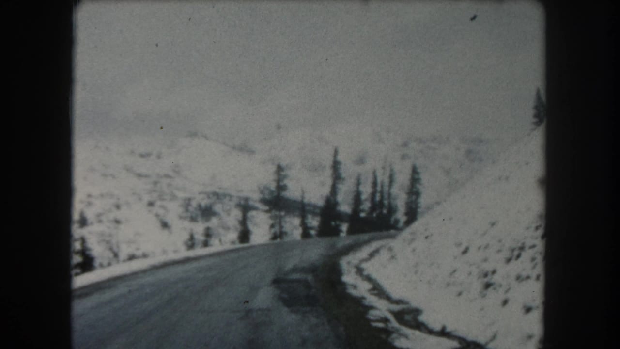 Summit County, Colorado road-trip footage from 1962 appears to show a paved mountain road bordered by snow and dark conifers.