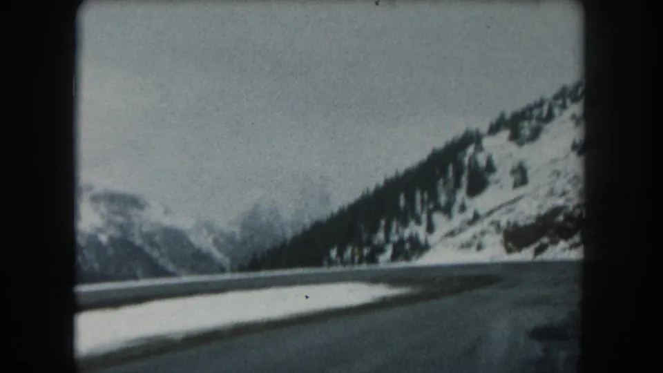 The final 1962 Colorado frame shows a low roadside view across snow toward dark evergreen-covered slopes and hazy winter mountains.