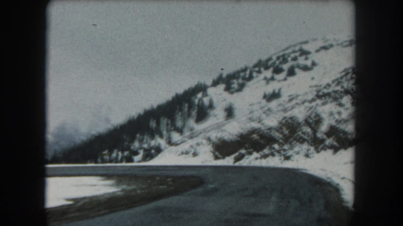 1962 8mm home-movie frame of a Summit County winter road bending along snow-covered Colorado mountain slopes.