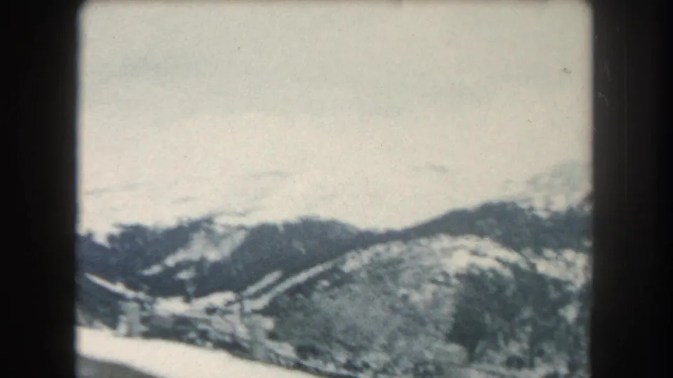 1962 Summit County, Colorado mountain view with snowy ridges, dark tree lines, and faded 8mm home-movie color.