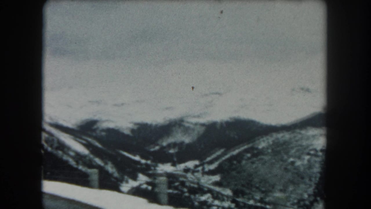 1962 Summit County, Colorado 8mm frame showing a snowy mountain road edge, guardrail posts, and distant forested slopes.