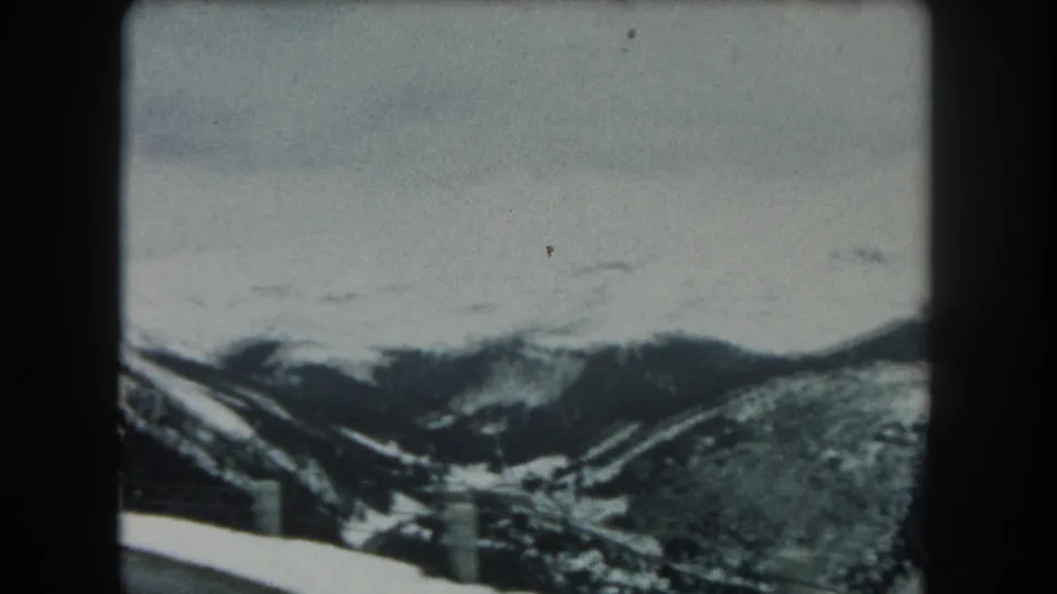 1962 Summit County, Colorado 8mm frame showing a snowy mountain road edge, guardrail posts, and distant forested slopes.