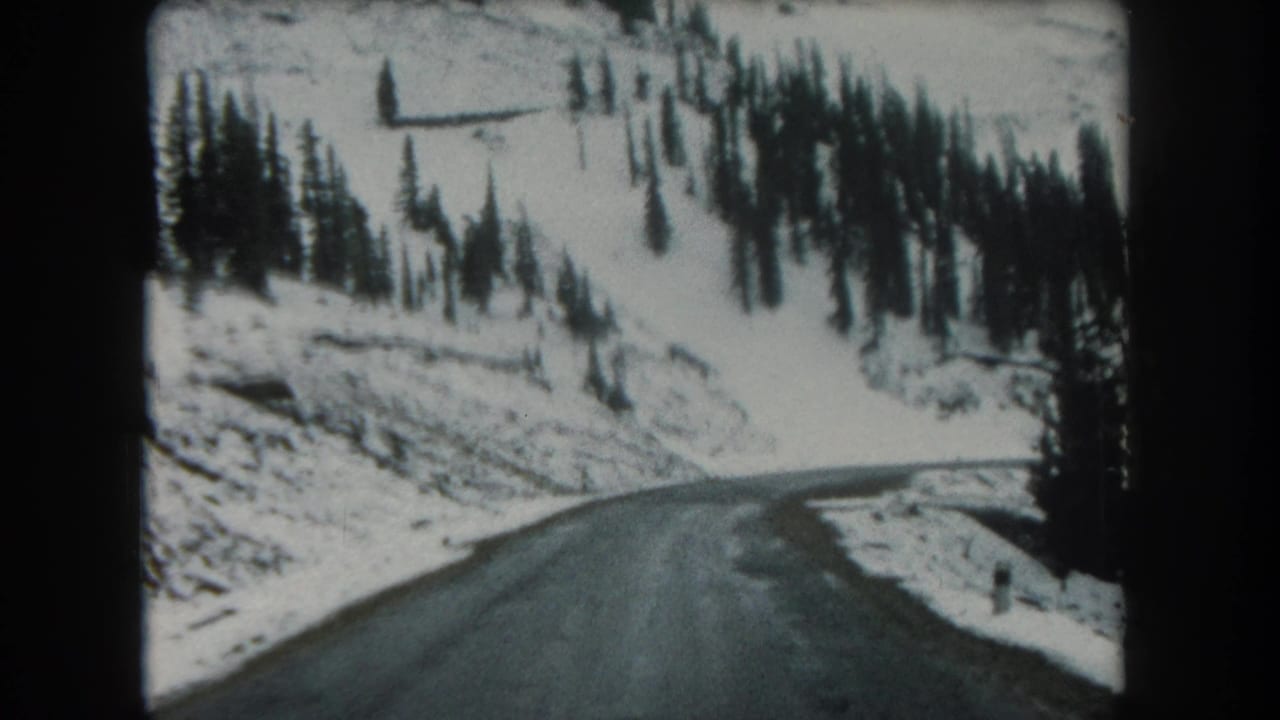 1962 8mm view of a wet narrow road bending through snow-covered evergreen hills in Summit County, Colorado.