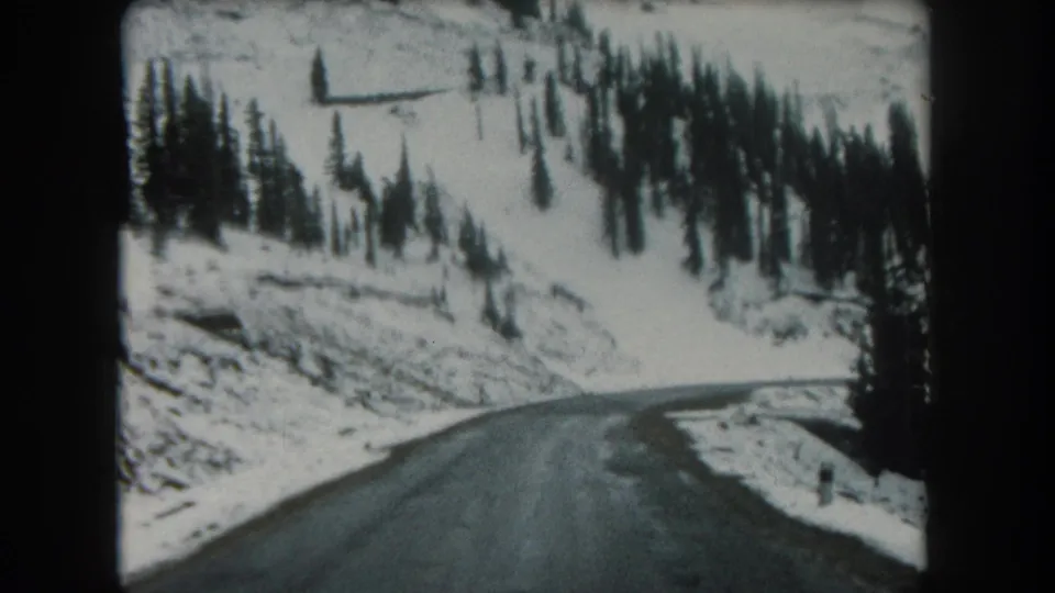 1962 8mm view of a wet narrow road bending through snow-covered evergreen hills in Summit County, Colorado.