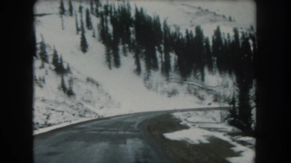 Final 1962 8mm travel frame of a wet road curving through snow-covered mountain forest in Summit County, Colorado.