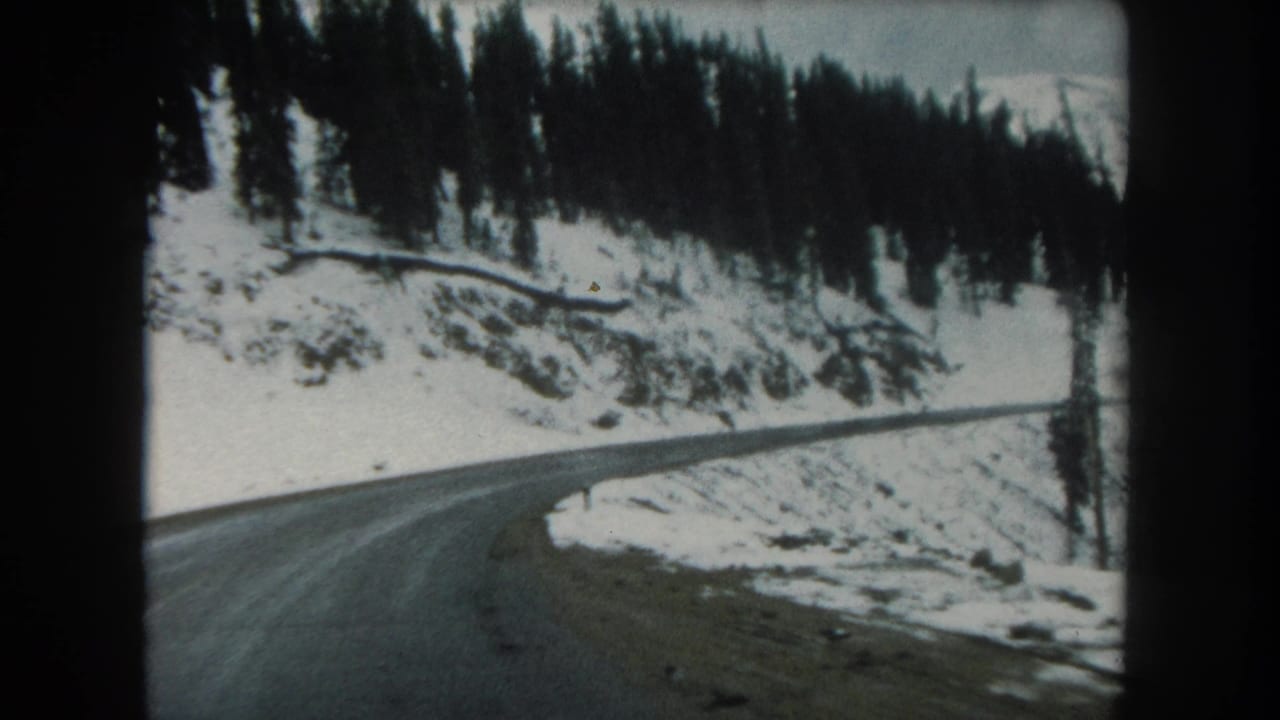 1962 Summit County, Colorado 8mm frame showing a wet road bending through snowy evergreen-covered hills.