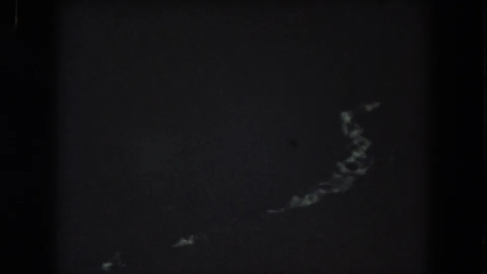 Dark end frame from the 8mm road clip, possibly a splice or transition, with a small bright curved trace.