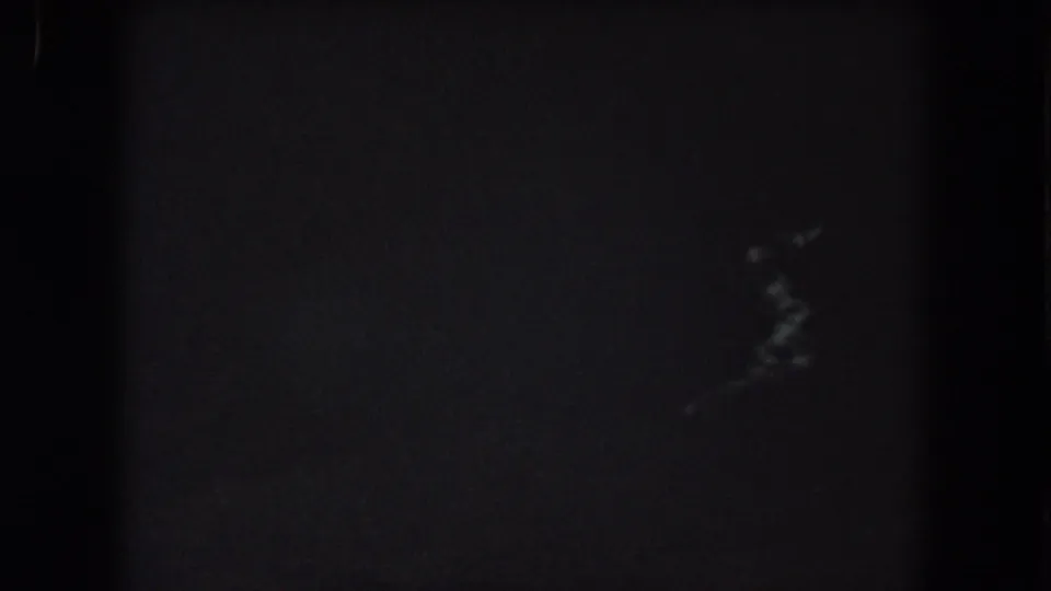 1962 Summit County nighttime home-movie frame showing small, blurred pale light streaks against a mostly black view.
