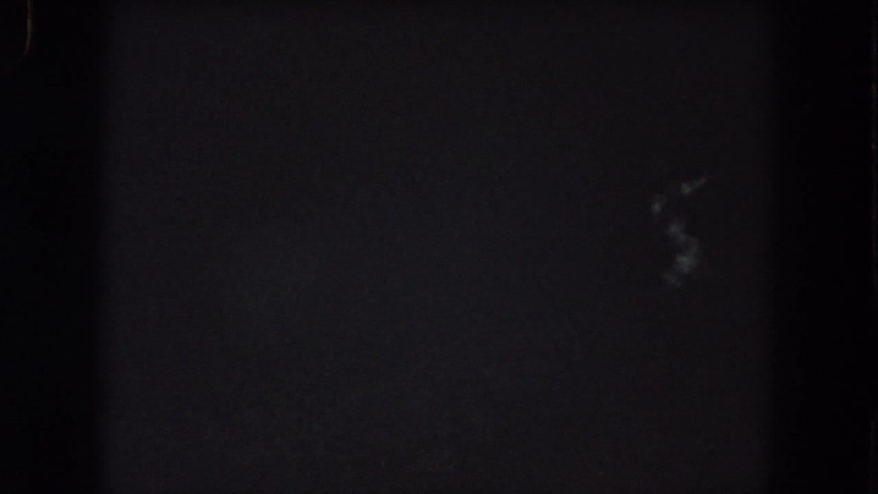 1962 Summit County night-drive frame with faint blurred light marks low in the view and dense 8mm grain.