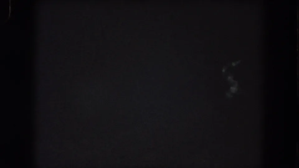 1962 Summit County night-drive frame with faint blurred light marks low in the view and dense 8mm grain.
