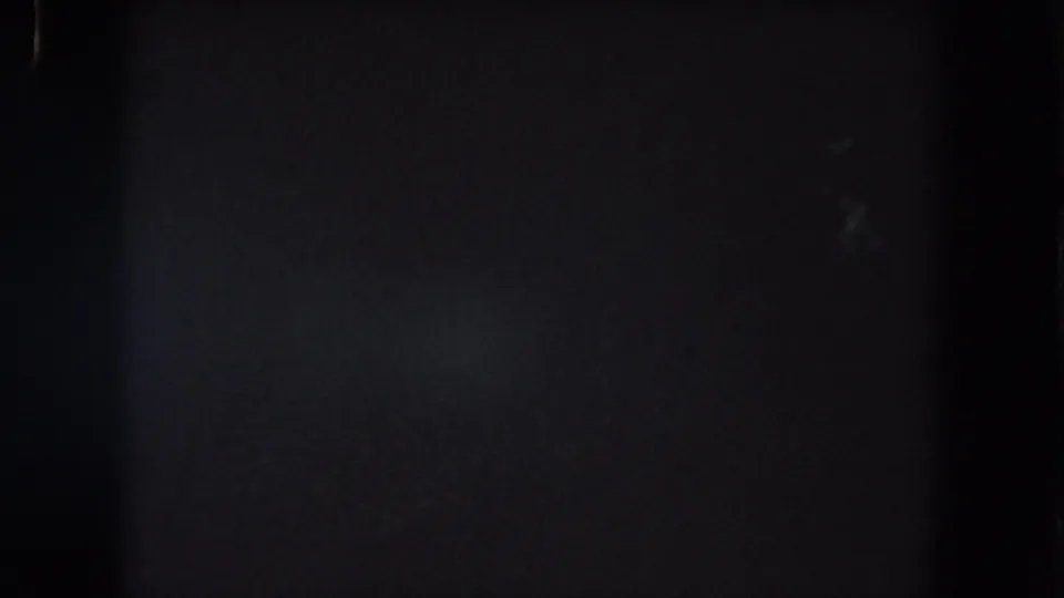 Underexposed Summit County 8mm night frame with a faint bluish area, visible grain, and dark vertical film divisions.