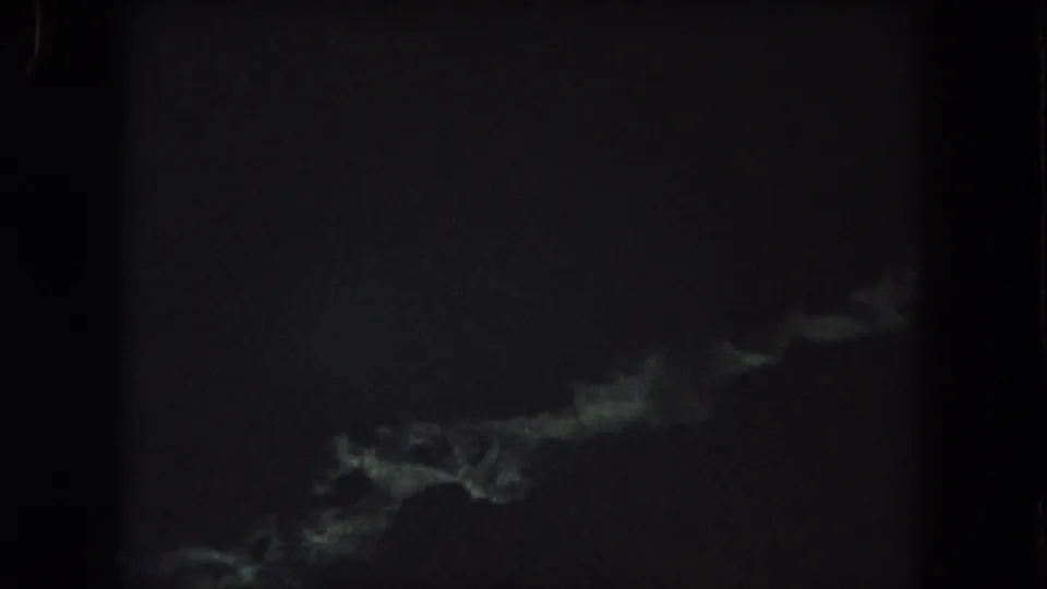Grainy 1962 8mm night footage showing a faint greenish-white streak low in the frame against a nearly black background.