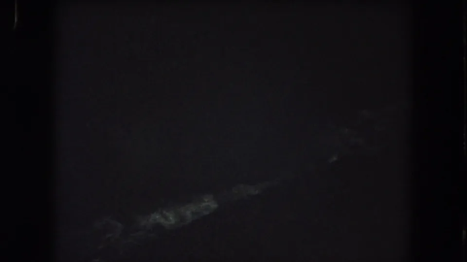Grainy 1962 Colorado night-sky frame with a pale wispy cloud form visible near the bottom.