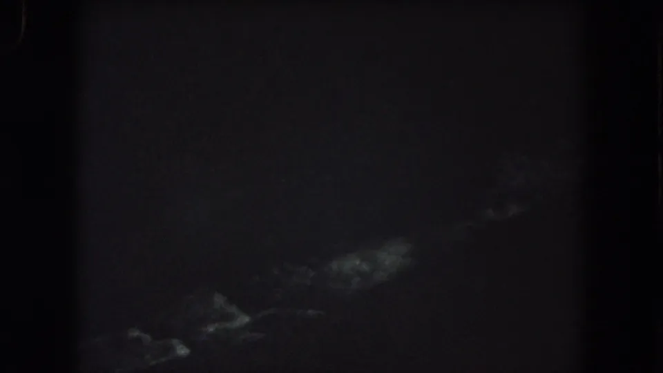 Underexposed 1962 8mm frame from Summit County showing indistinct pale forms in darkness, possibly trees or terrain.