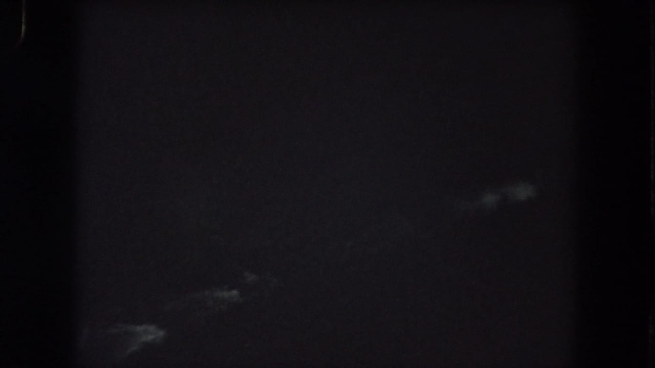 Mostly dark frame with faint pale streaks and heavy film grain.