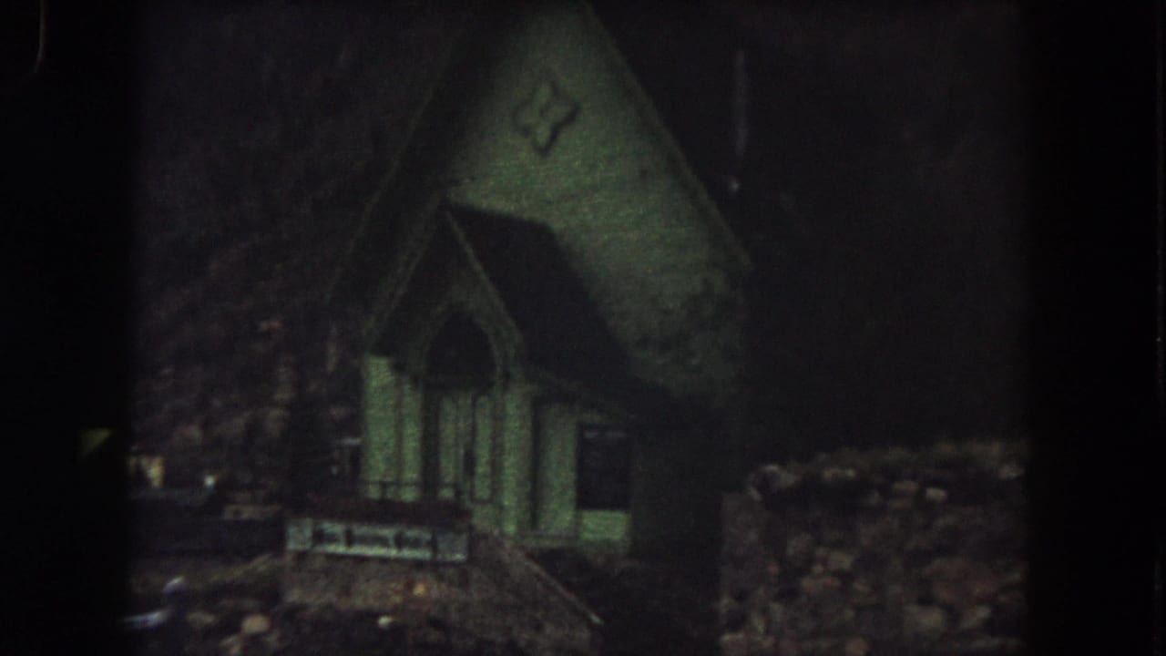 1962 Summit County, Colorado 8mm frame showing a small green church exterior at night, dimly lit against darkness.