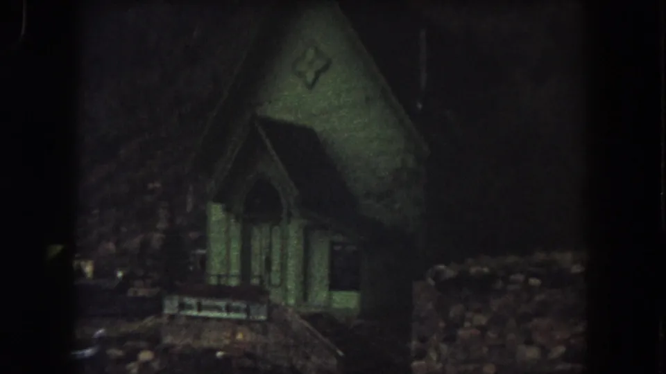 1962 Summit County, Colorado 8mm frame showing a small green church exterior at night, dimly lit against darkness.