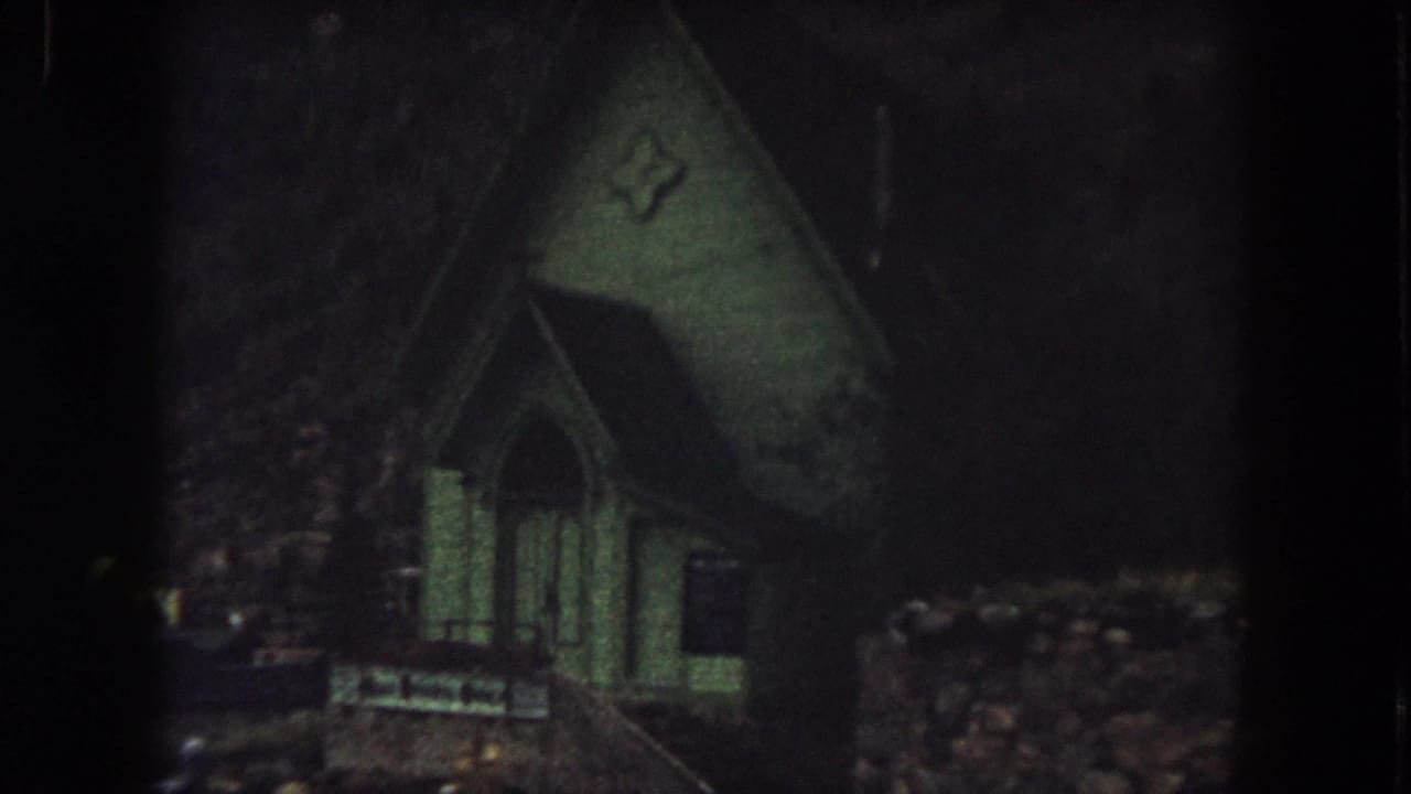 Dim nighttime view of a small church entrance and dark surrounding ground.