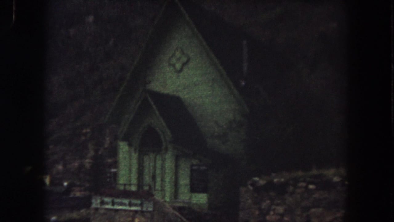 1962 Summit County, Colorado 8mm still showing the green church facade closer in frame, with deep shadows around it.