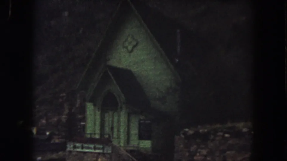 1962 Summit County, Colorado 8mm still showing the green church facade closer in frame, with deep shadows around it.