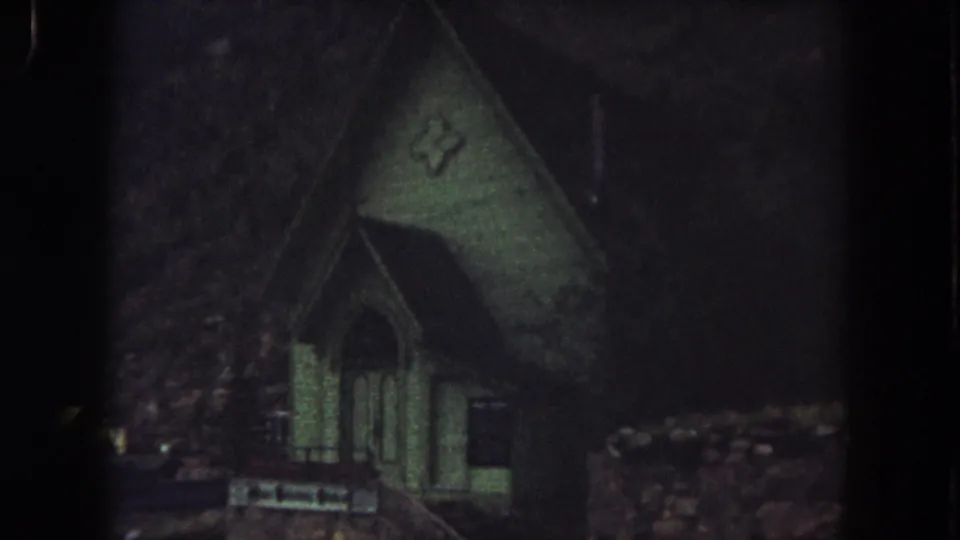 1962 Summit County view of a small green church with an arched entrance, cross emblem, and hillside surroundings.