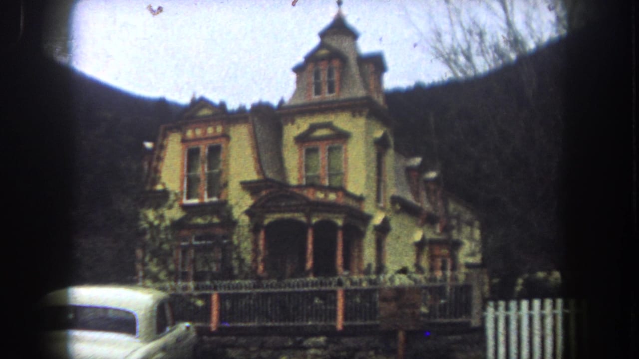 1962 Summit County home-movie frame showing the yellow Victorian-style house from a slightly shifted roadside angle.