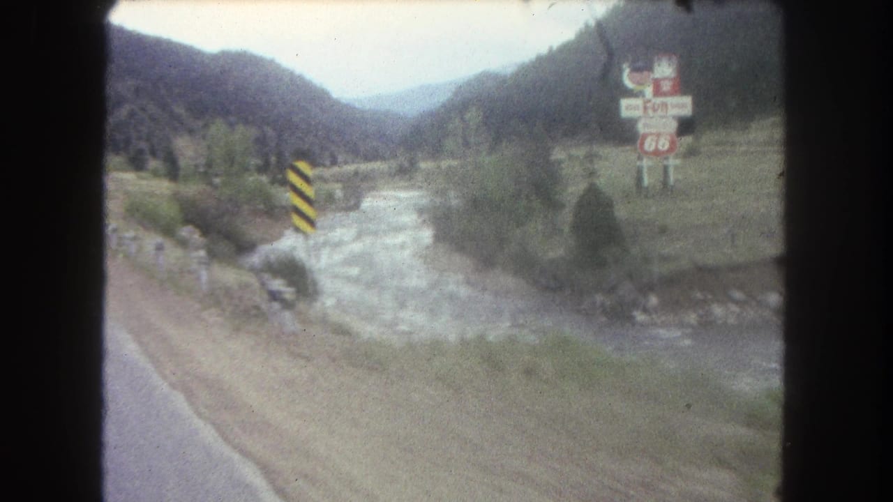 1962 Summit County, Colorado 8mm frame showing a road along a river valley with mountain slopes and roadside signage.