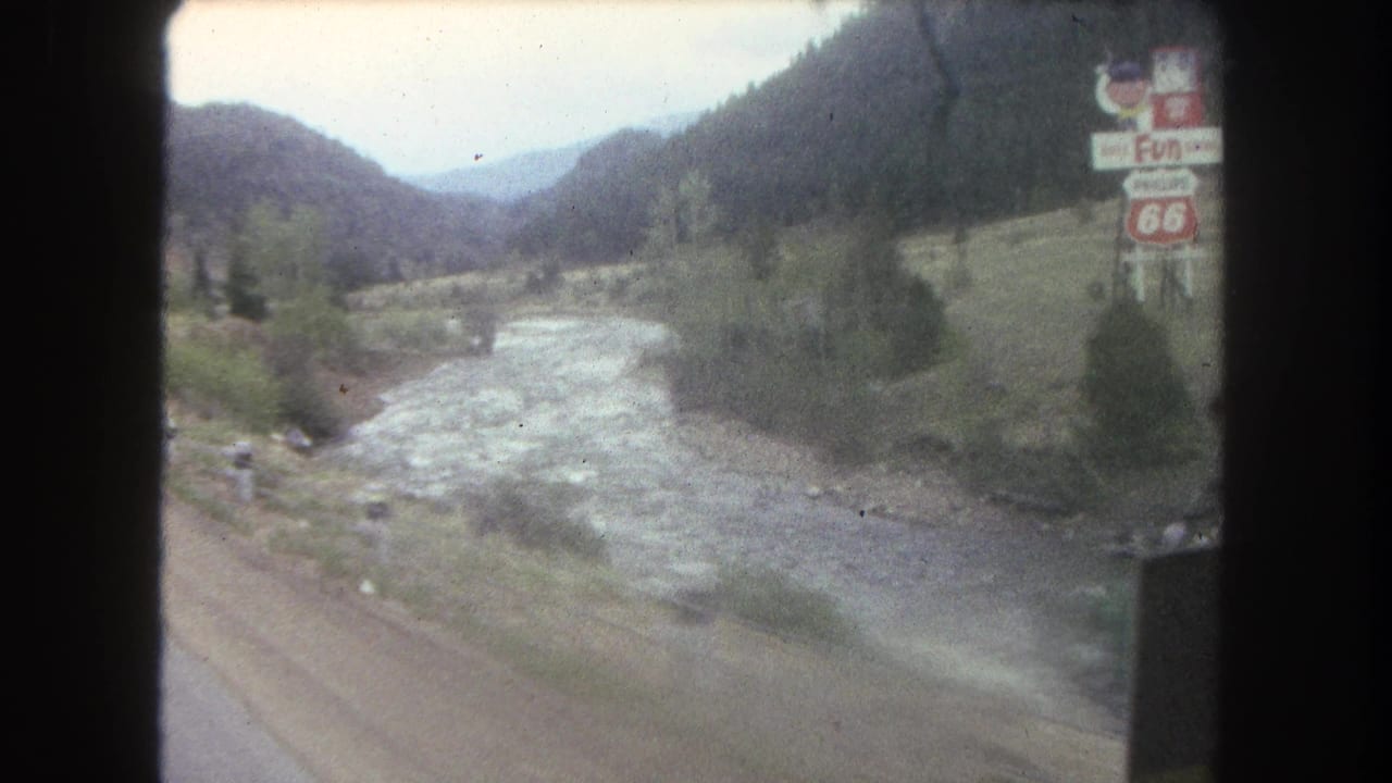 1962 Summit County, Colorado 8mm view of a river running beside a mountain road with distant traffic and roadside signage.