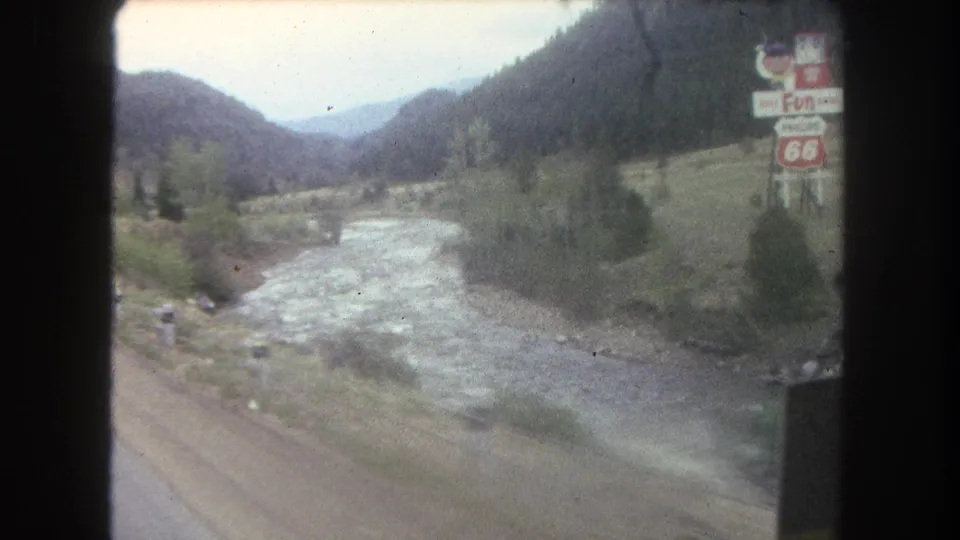 1962 Summit County, Colorado 8mm view of a river running beside a mountain road with distant traffic and roadside signage.