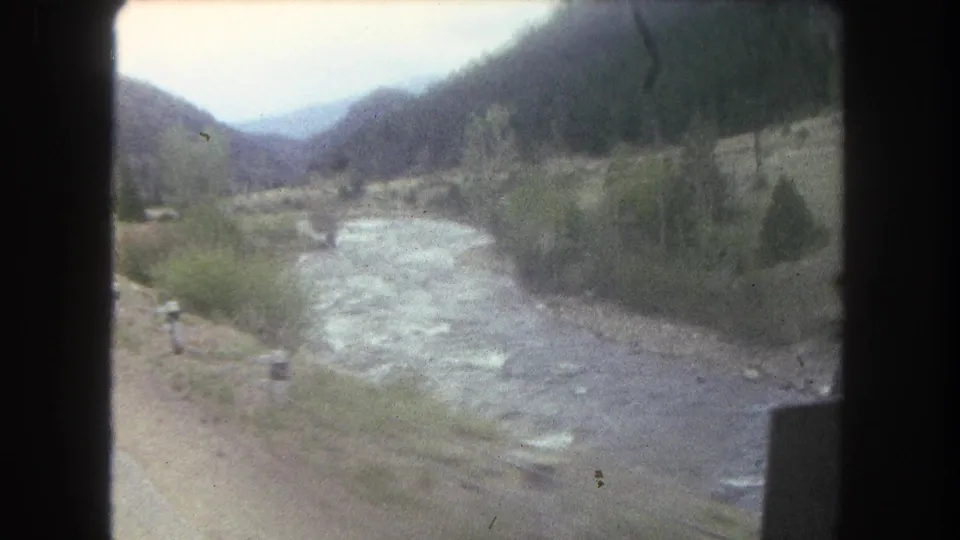 1962 Summit County, Colorado home-movie frame of a road curving along a river through a green mountain valley.