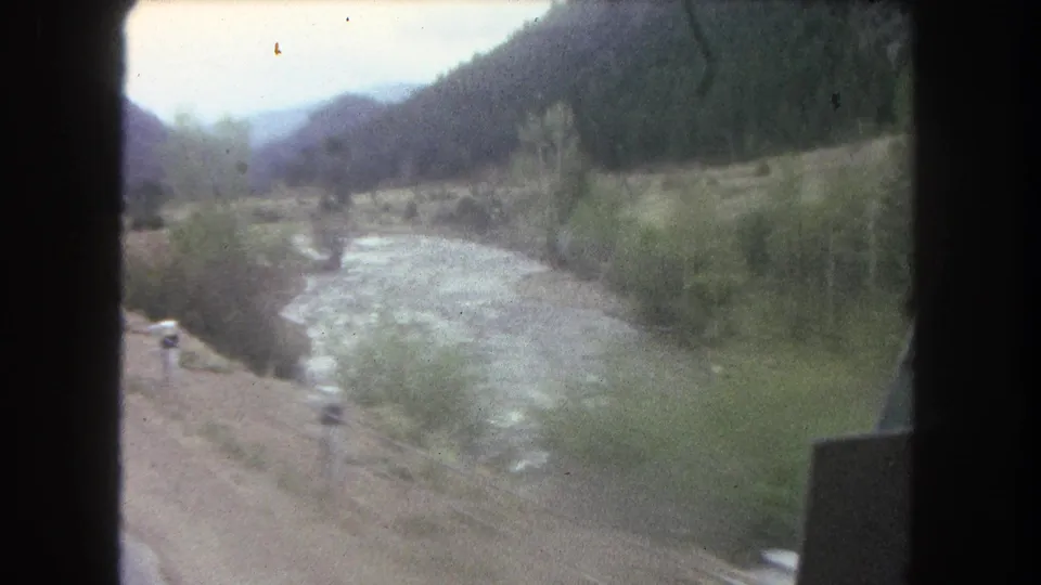 1962 Summit County, Colorado 8mm frame showing a moving-vehicle view along a river road in a mountain valley.