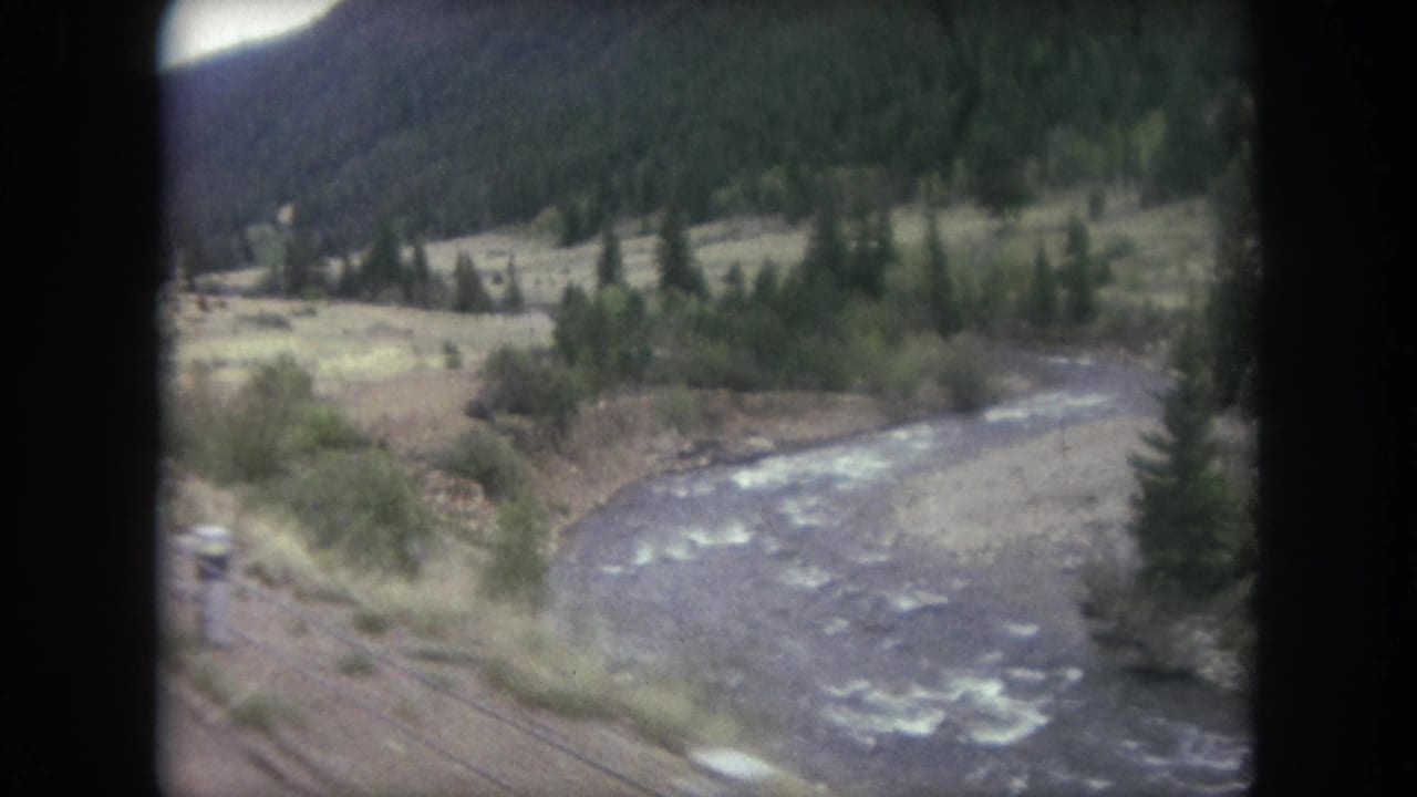 1962 8mm view near Winter Park, Colorado, looking from a moving train toward a river, tracks, trees, and mountain valley.