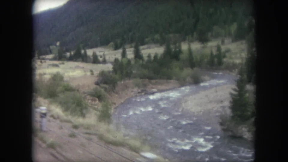 1962 8mm view near Winter Park, Colorado, looking from a moving train toward a river, tracks, trees, and mountain valley.