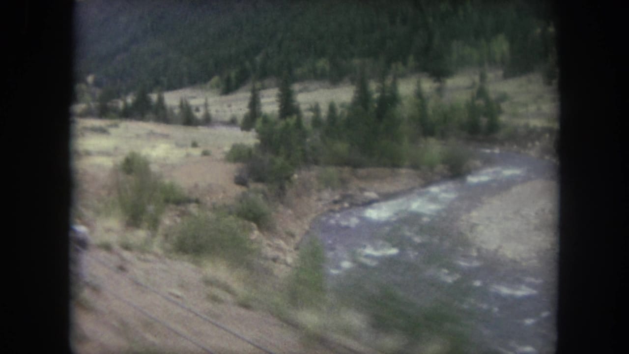 River bend and valley brush seen from a moving rail-side viewpoint.