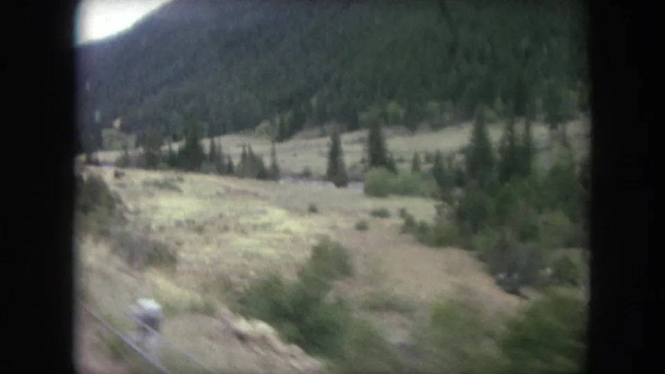 Final 8mm frame of the Winter Park train view, with open valley ground, brush, trees, river corridor, and mountain backdrop.