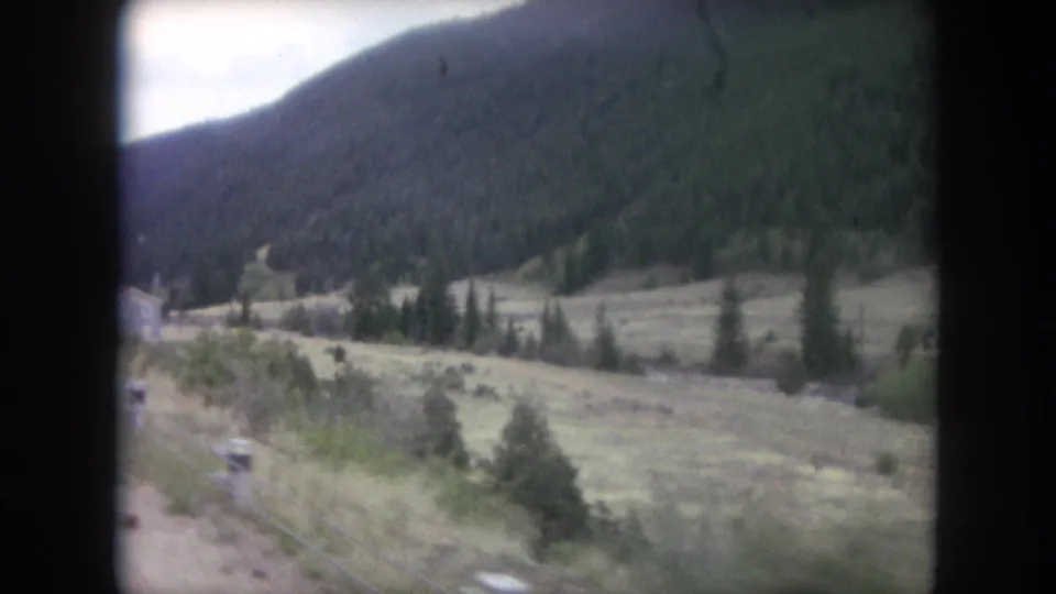 1962 Winter Park, Colorado home-movie frame showing a blurred travel view of field, evergreens, and wooded mountainside.