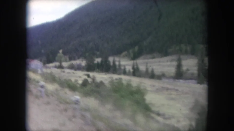 1962 Winter Park, Colorado frame showing rural valley terrain with shrubs, evergreens, and a wooded mountain in the background.