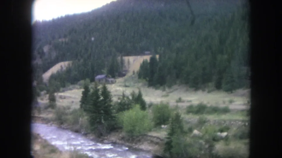1962 Winter Park, Colorado home-movie still showing a river bend and cabin-like structure below a forested mountain slope.
