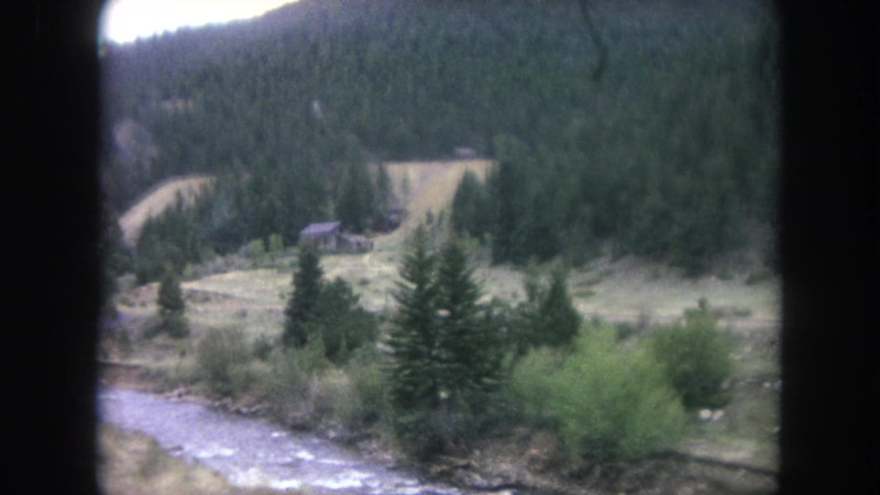 1962 Winter Park 8mm frame showing a creek, brush, evergreens, and a forested Colorado hillside from a moving car.